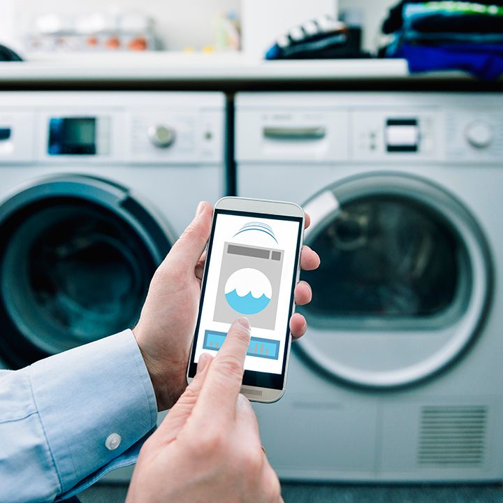 Mann mit Smartphone zur Steuerung von Waschmaschine und Trockner.
