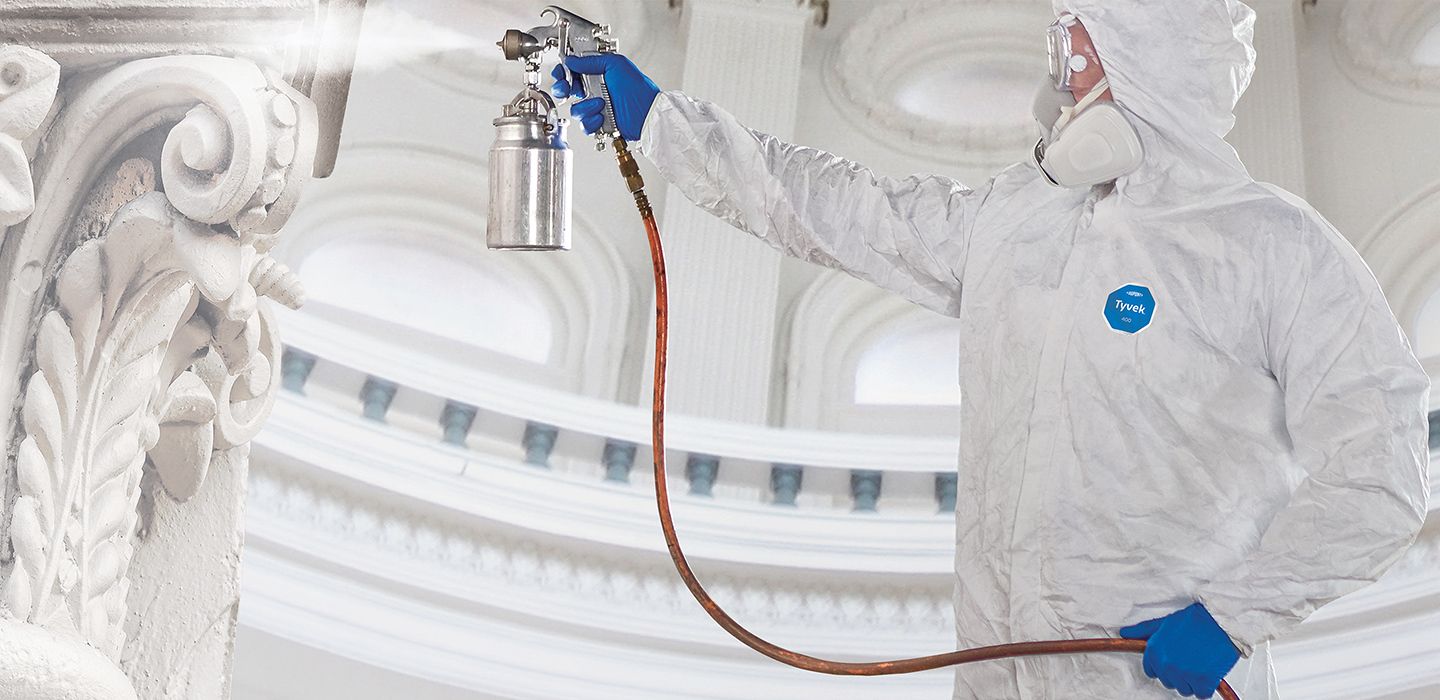 Painter in protective suit using commercial sprayer.