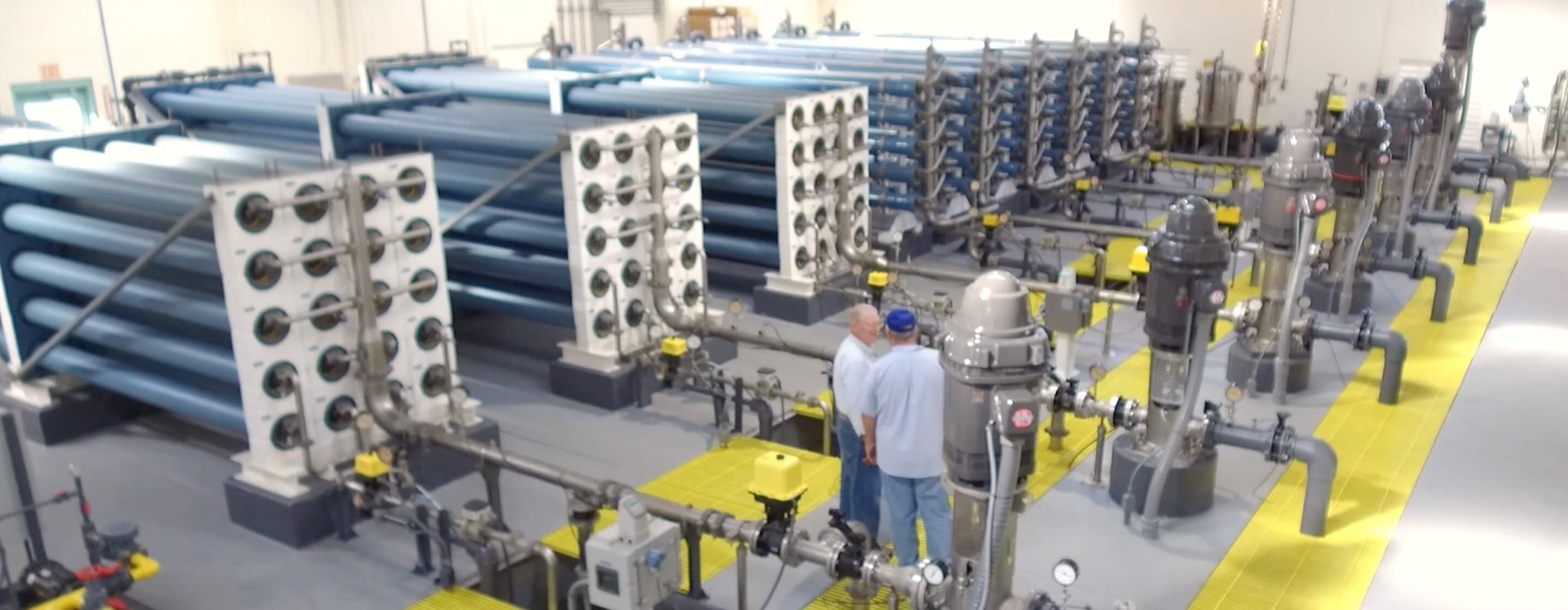 Multiple arrays of stacked reverse osmosis elements in a industrial water-treatment room, with two men consulting together