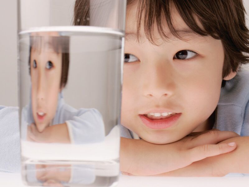 Young boy looking through a glass containing clean, clear household water