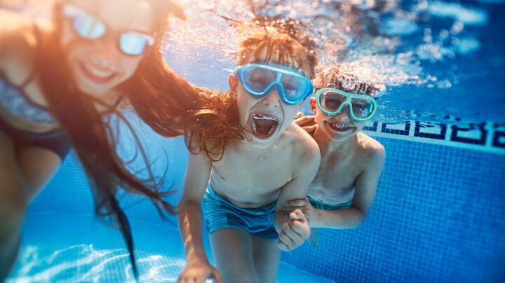 Underwater view of three smiling children with swimming goggles playing and blowing bubbles in a swimming pool