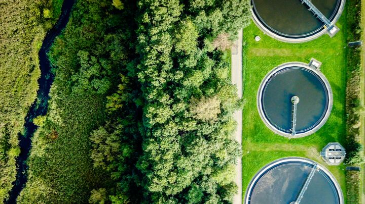 Aerial view of a municipal water treatment plant's settling tanks next to a dense bank of trees and a brook