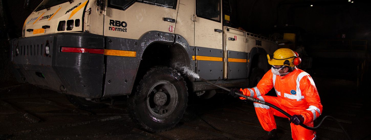 Trabajador minero limpiando vehículo industrial con equipo de protección.
