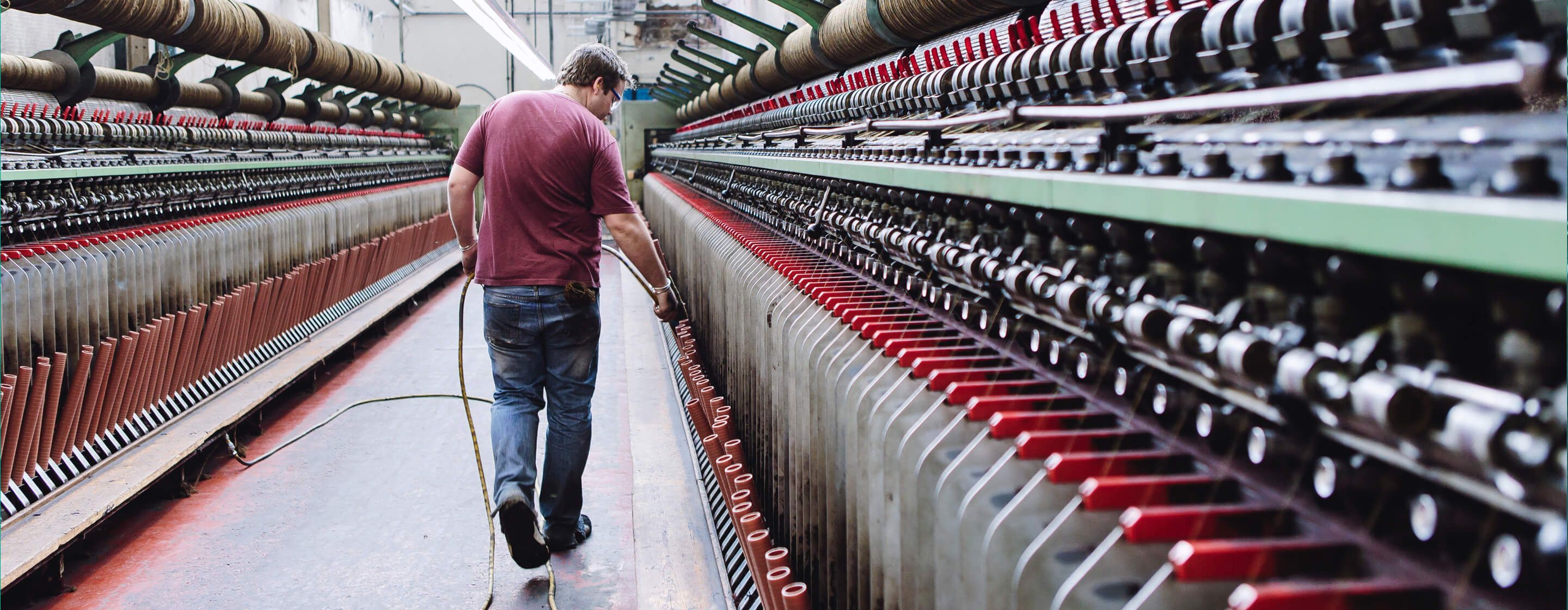 Man in t-shirt and jeans tending to large industrial textile looms in the textiles industry