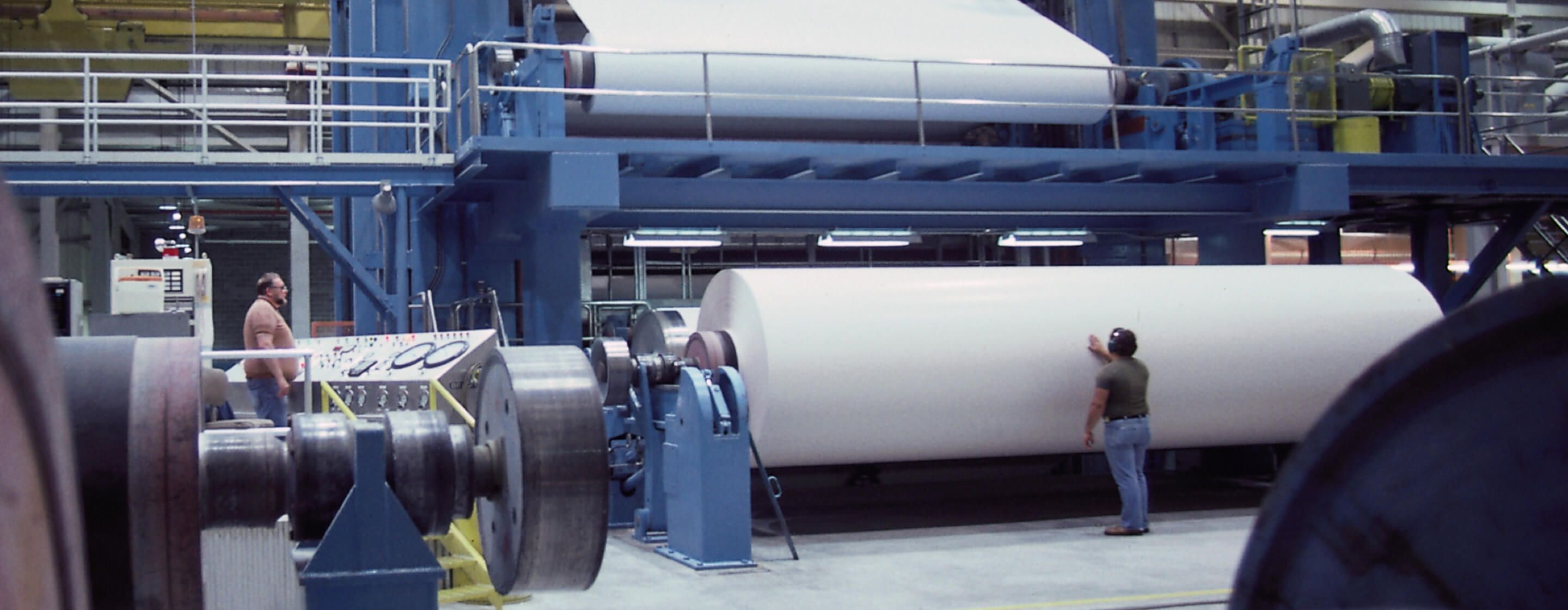 Man inspecting massive roll of paper in a pulp and paper plant