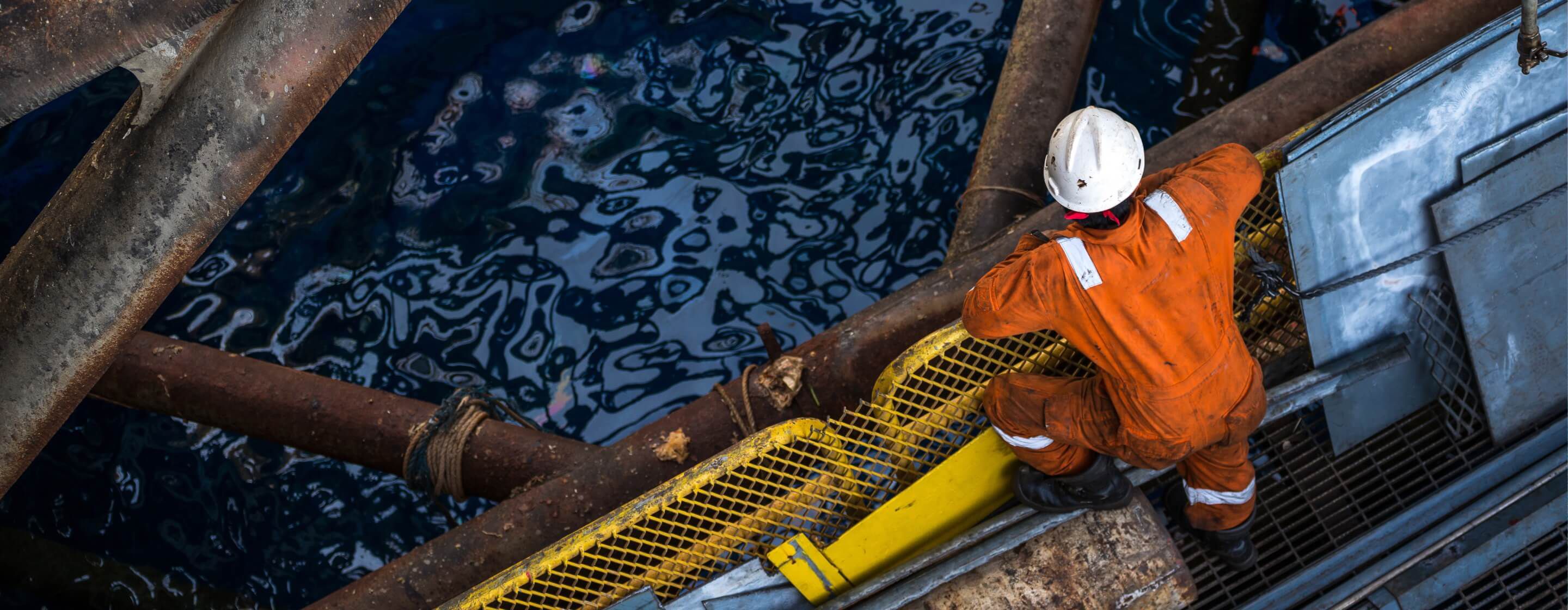 Overhead view of an offshore oil-rig worker in a jumpsuit, hard hat, and work boots looking down into ocean water