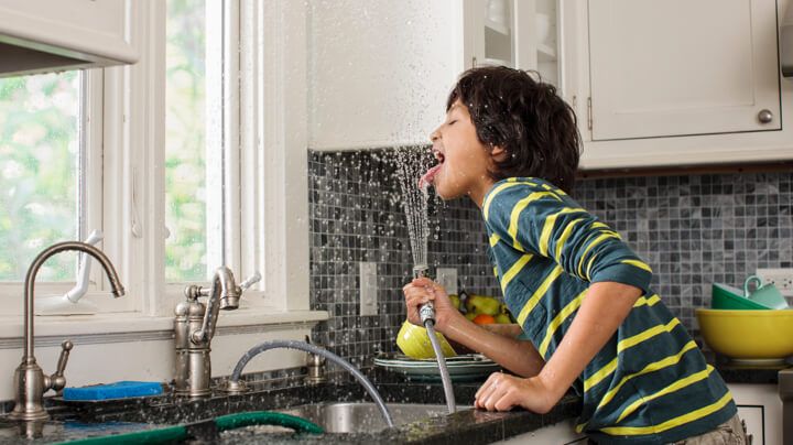男孩喝着厨房水槽喷雾器里的清洁家用水。