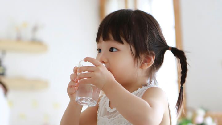 Young girl in a sunny room sips from a glass full of safe and clean drinking water.