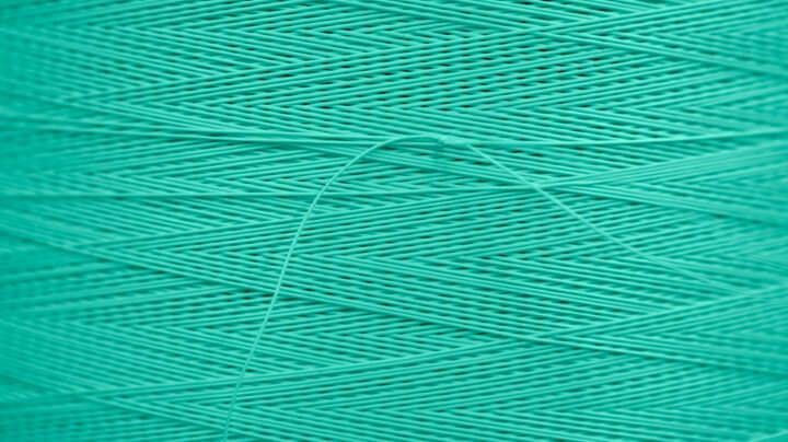 Extreme close-up of a spool of turquoise-colored thread produced by, and for use in, the textiles industry.